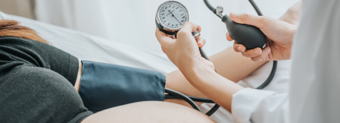 Doctor checking blood pressure of a pregnant woman patient with sphygmomanometer in bed